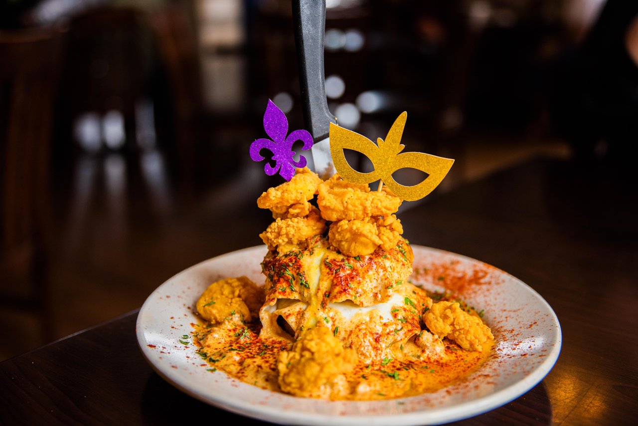 A Cajun pasta dish topped with fried shrimp, jalapeños, and a Mardi Gras mask garnish at a Lake Charles restaurant.